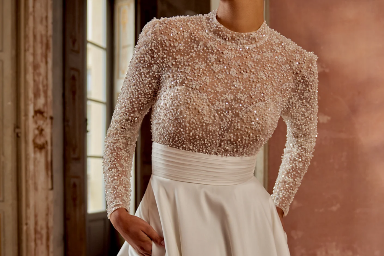 Bride wearing a high-neck wedding gown with long sleeves and intricate beaded embellishments on the bodice.